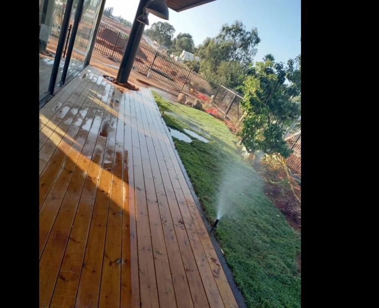 Wooden deck overlooking a grassy yard with brick walls and green trees under clear blue sky