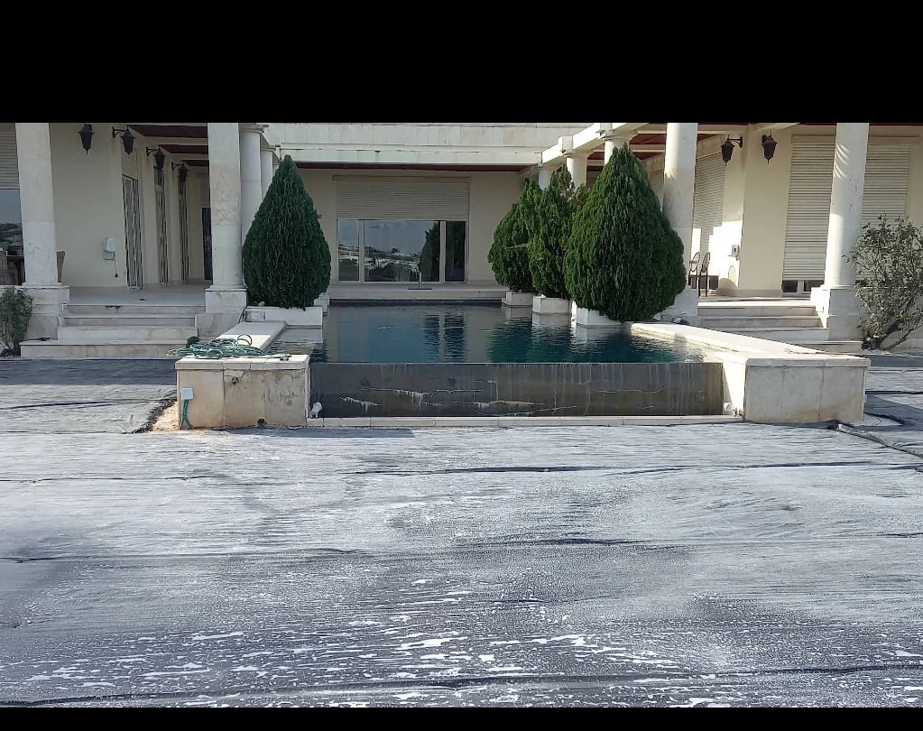 Modern courtyard with rectangular reflecting pool, green topiaries, white columns, and contemporary architecture
